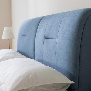 blue-bedframe-against-the-wall-with-two-pillows-against-it-and-a-lamp-on-the-side